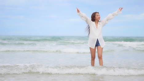 A-beautiful-young-woman-walks-through-the-incoming-surf-raises-her-arms-and-hands-in-joy