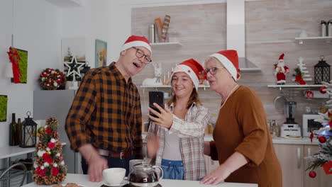 Familia-Feliz-Con-Sombrero-De-Santa-Saludando-A-Amigos-Remotos-Durante-Una-Reunión-De-Videollamada-En-Línea-Usando-El-Teléfono