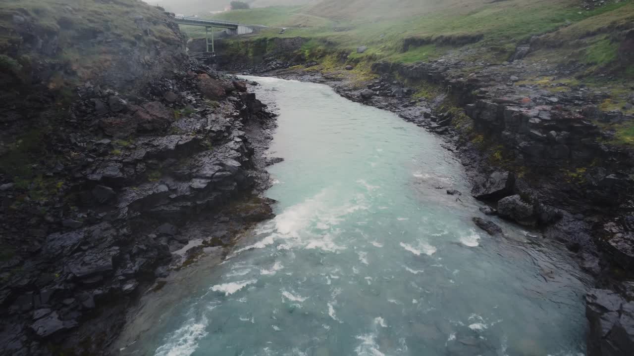 tomada de un avión no tripulado de un río islandés furioso y campos verdes sobre las rocas negras y rápidos