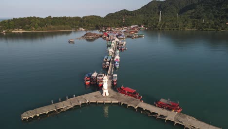 Fast-aerial-tilt-up-and-out-of-the-sun-hitting-the-Bang-Bao-fishing-pier-along-the-coast-of-Koh-Chang,-Thailand