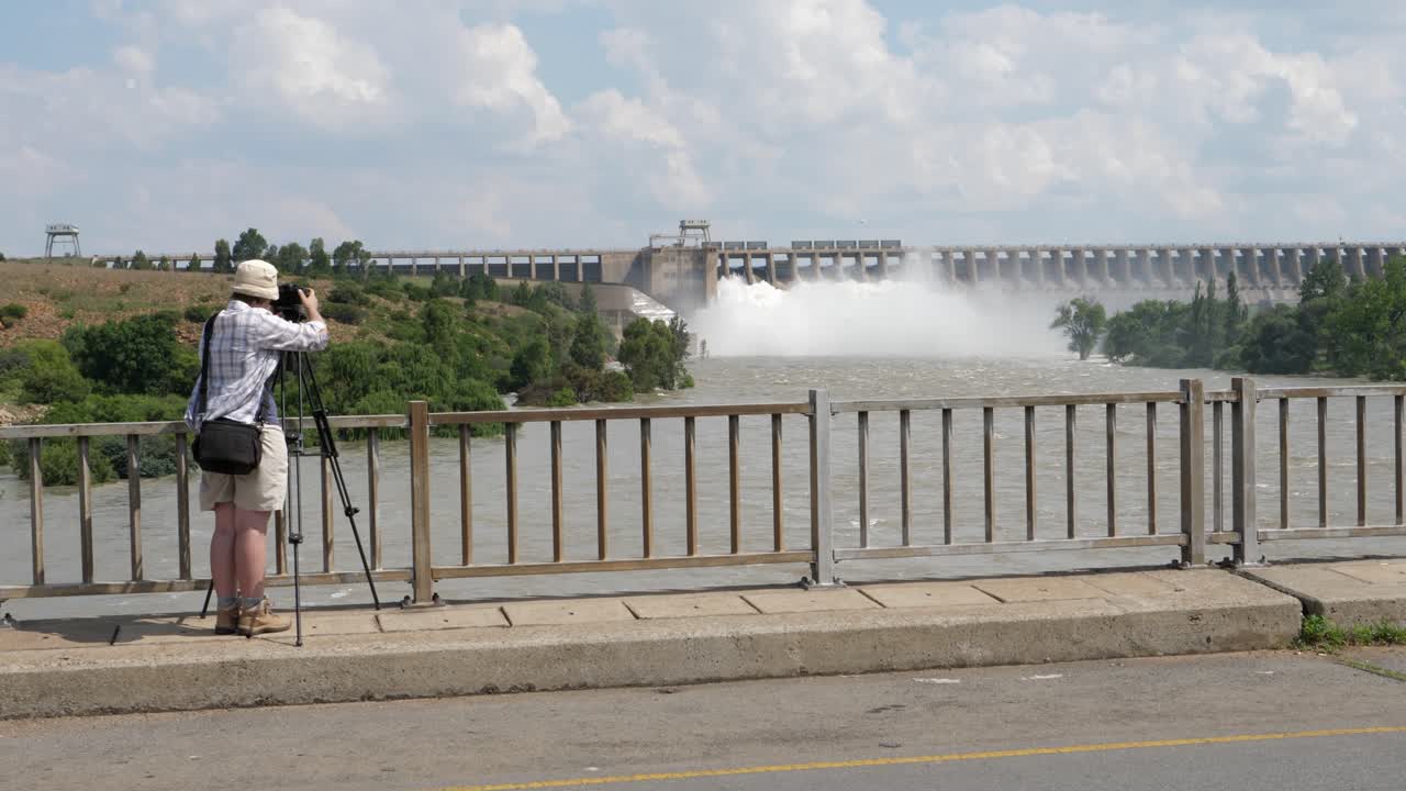 다리 위의 사진작가가 홍수 물을 방출하는 발 강 댐을 촬영합니다.