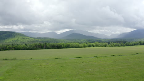 aerial view of the lush green adirondack mountains with storm clouds overhead - rising drone shot