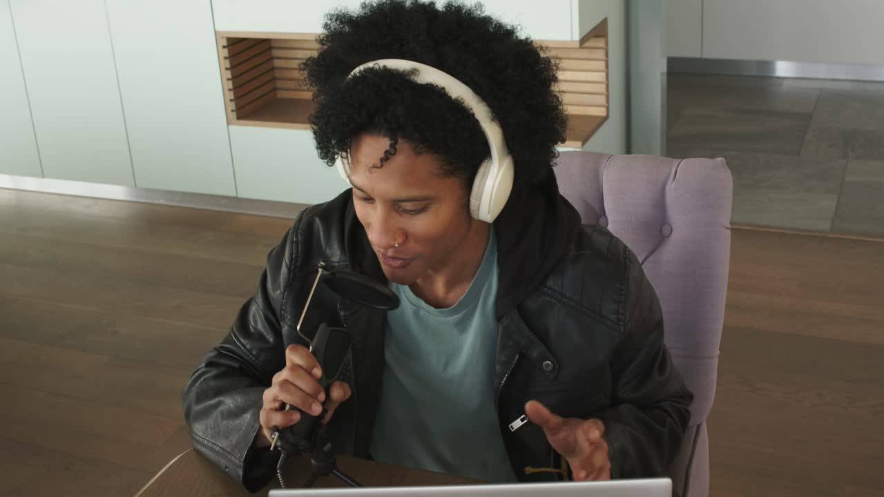 Mid adult man placing laptop and adjusting mic for podcast while typing and speaking in kitchen