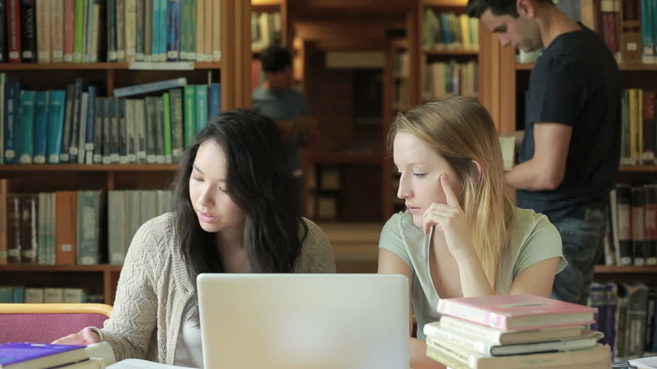 estudiantes viendo algo en la computadora portátil en la biblioteca