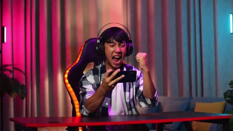 excited asian teen boy gamer celebrates victory while playing video game on smartphone