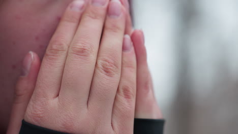 vista de cerca del rostro de una mujer joven que siente frío en invierno, frotándose las manos para calentarse, nariz roja y piel seca resaltan las duras condiciones climáticas, el fondo borroso de árboles desnudos mejora
