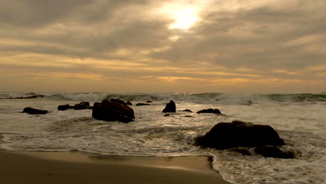 Pequeñas-Olas-Rodando-Sobre-Pequeñas-Rocas-En-La-Playa-Durante-La-Hermosa-Puesta-De-Sol-Y-Cielos-Dramáticos,-Hora-Dorada