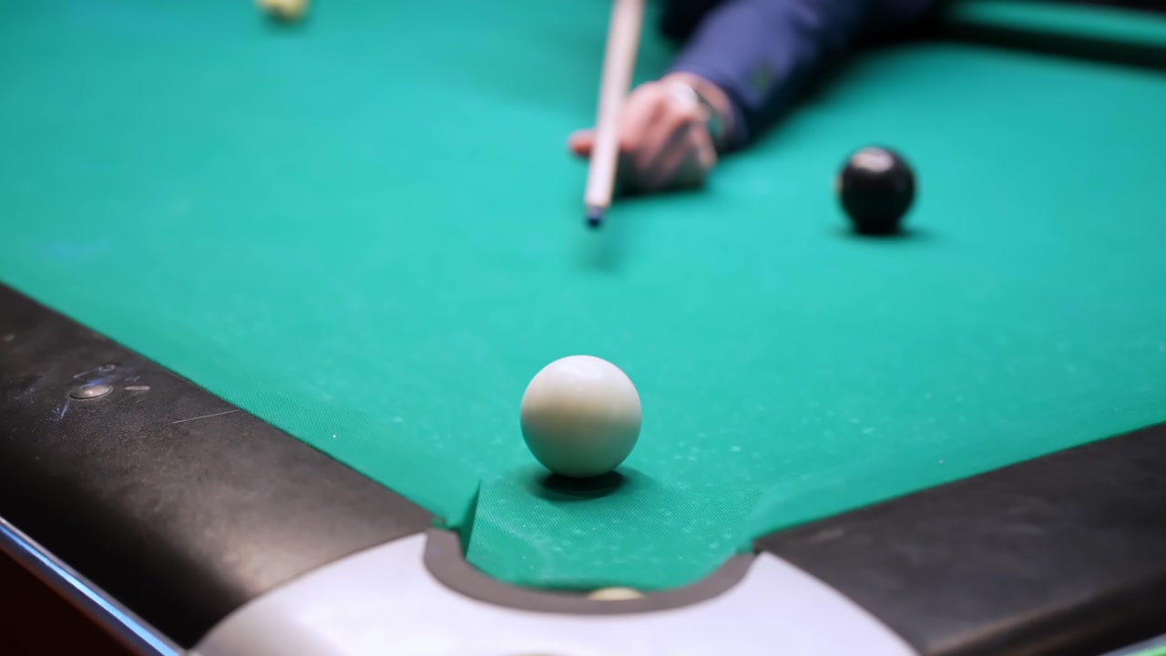 Accidental scratch as the cue ball and yellow stripe drop together into a side pocket on a pool table; close-up green felt with player hand and eight visible in the background.