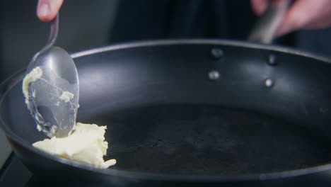 chef cook puts butter in frying pan on stove