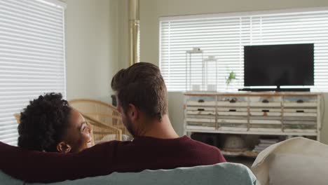 Video-of-back-view-of-happy-diverse-couple-drinking-coffee-and-watching-tv-with-copy-space