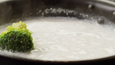 cooking broccoli in a pan with white sauce