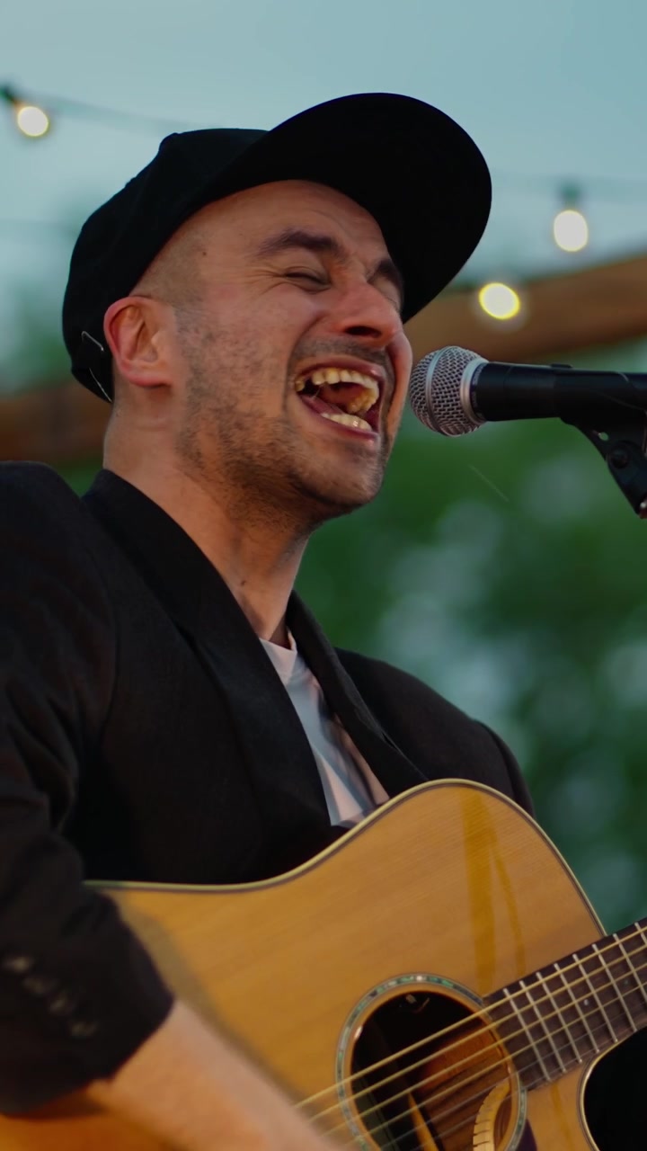 Man Singing and Playing Acoustic Guitar at an Outdoor Event