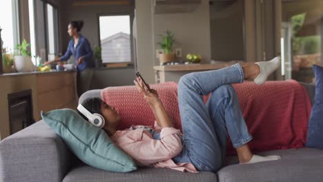 Vídeo-De-Una-Mujer-Birracial-Relajada-Con-Auriculares-Tumbada-En-El-Sofá-Y-Usando-Un-Teléfono-Inteligente