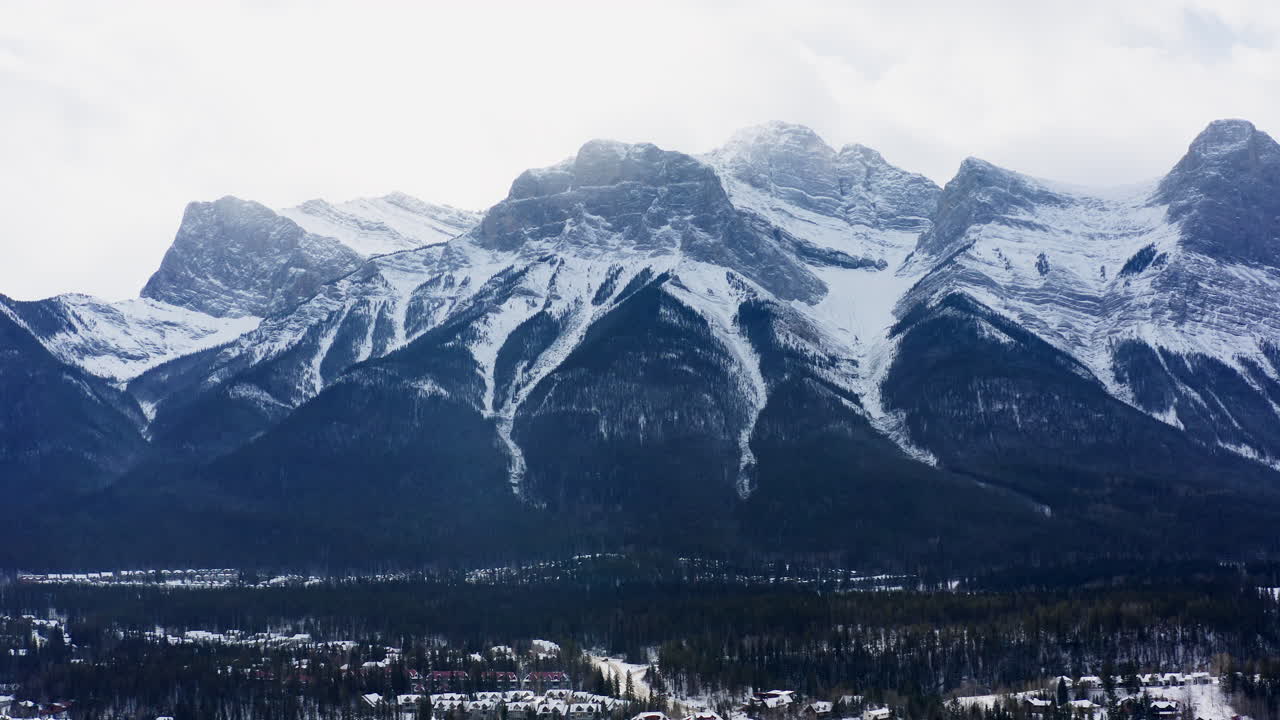 A dramatic drone fly-out reveals snow-covered peaks and the quiet town of Canmore nestled below the towering Banff mountains.
