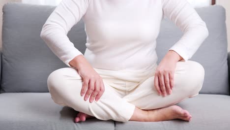 Young-woman-in-cross-legged-position-on-the-sofa-performing-self-massage-on-her-legs