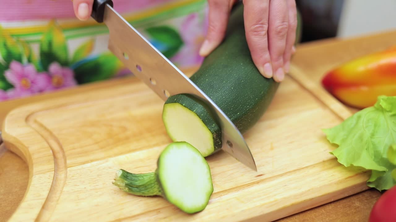 Women's hands Housewives cut with a knife fresh zucchini on the cutting Board of the kitchen table