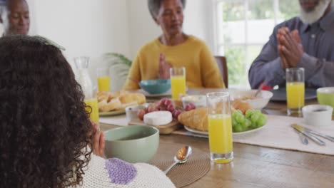 video de padres afroamericanos felices, hija y abuelos diciendo la gracia en la mesa de la cena