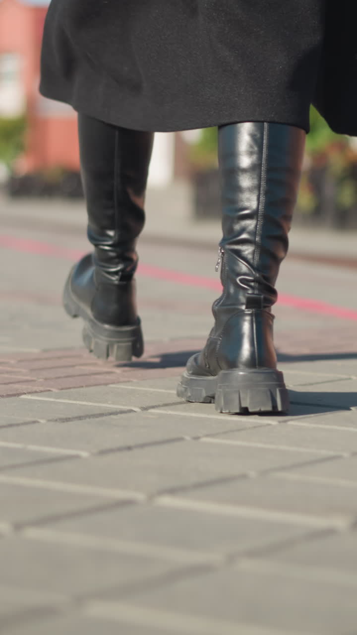 vista de la pierna trasera de una persona con botas negras y abrigo sosteniendo un maletín negro, paseando por un camino entrelazado con estructura urbana y figura en movimiento borrosa en el fondo