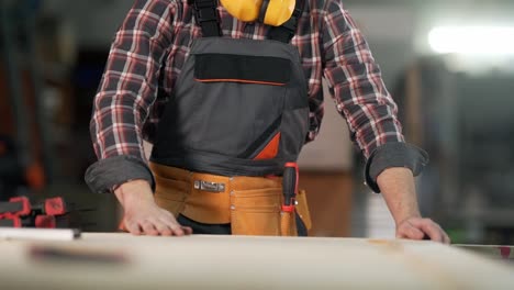 full face portrait of a young bearded carpenter blowing dust from a wooden product