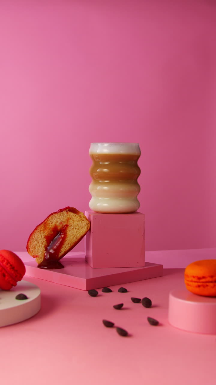 A hand lifts a foamy cappuccino from a sculptural pedestal, surrounded by a sliced Berliner donut, macarons, and photo props, perfect for lifestyle food branding and café product visuals