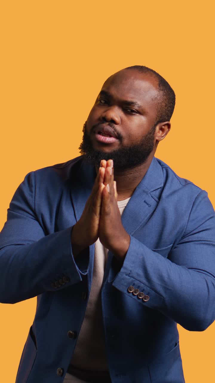 African American Man Pleading with Hands Together on Orange Background
