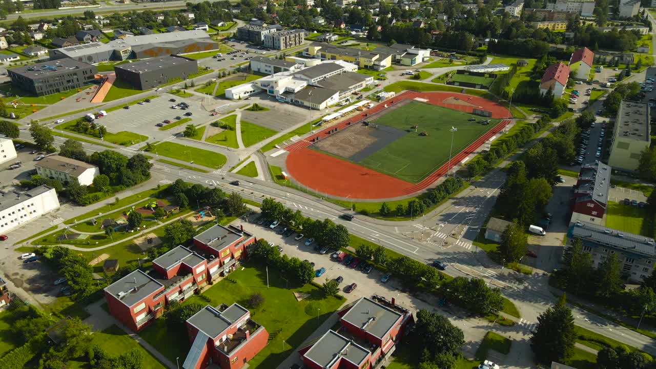 Aerial drone footage orbiting and flying around in front of a large green and red colored soccer field or stadium that is under construction or being renovated with workers removing green grass. sunny