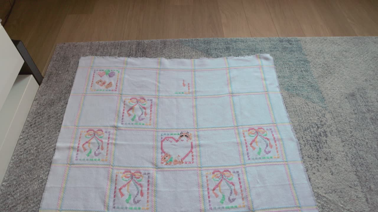 tilting shot revealing a finished cross-stitch baby blanket on the ground