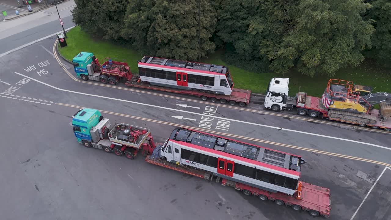 Drone view of Metro tram trains on lorries at Gordano Motorway Services, highlighting large-scale transit operations, Bristol UK, October 2024