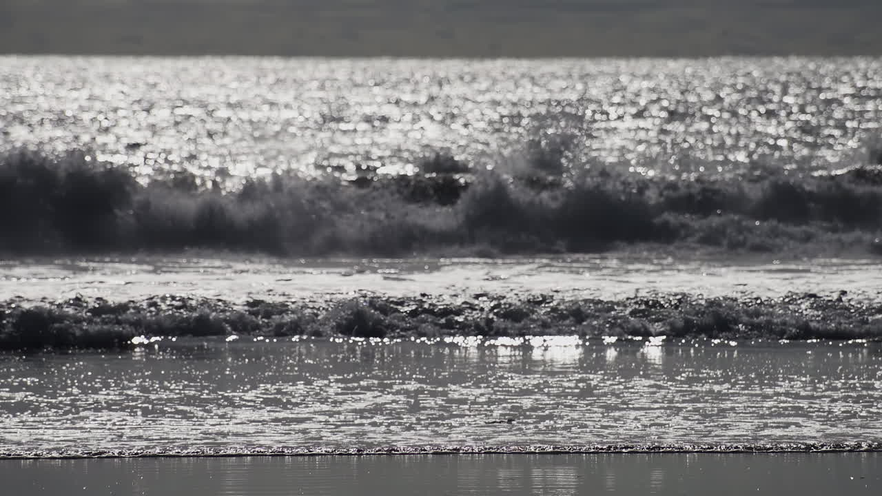 Ocean waves glisten under the sunlight, creating a sparkling reflection on the water surface