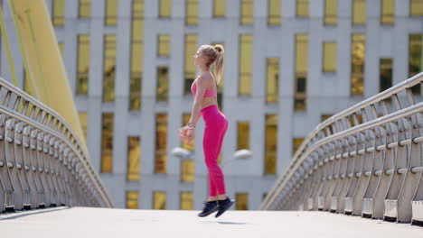 young fit woman in pink sportswear works out on bridge, wide side view