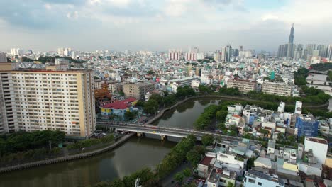 areal drone approaching a bridge and canal dividing two parts of the city in ho chi minh vietnam with landmark 81 in the distance on a cloudy afternoon