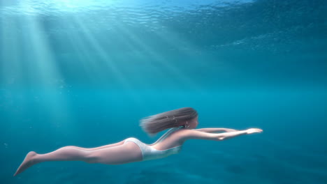 woman gracefully swimming underwater in clear blue water with sun rays