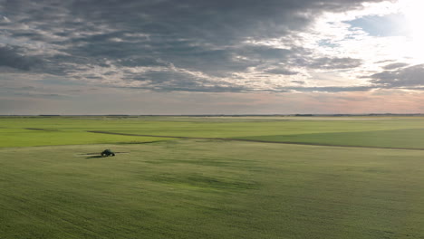 Sensational-scenic-flight-above-green-farmland-towards-industrial-farming-machine-spraying-fungicide-on-cereal-crops-in-flat-expansive-countryside,-Saskatchewan,-Canada,-overhead-aerial-approach