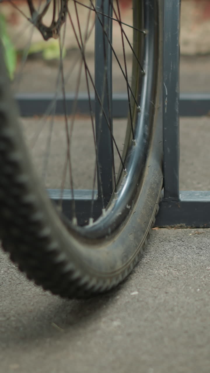 금속 자전거 랙에 주차 된 자전거 바의 클로즈업, 스피크와 프레임 세부 사항을 처, 배경은 추가 자전거와 흐릿한 초록색을 특징으로합니다.