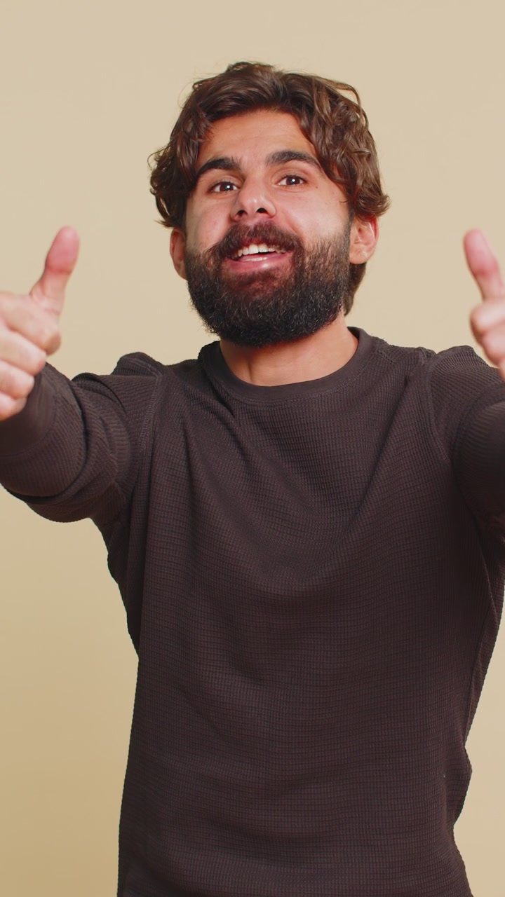 Uomo felice alza il pollice in su, approva qualcosa e dà una risposta positiva su sfondo beige.