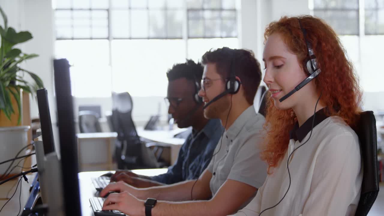 Side view of young cool mixed-race call center team calling and sitting at desk of modern office 4k