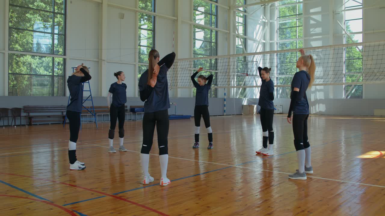 バレーボールチームが体育館でストレッチをしている。