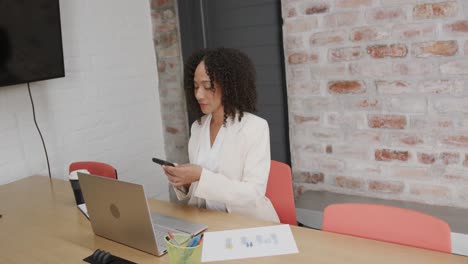 Glückliche-Biraziale-Geschäftsfrau,-Die-Im-Büro-Einen-Laptop-Benutzt-Und-Auf-Dem-Smartphone-Spricht,-In-Zeitlupe