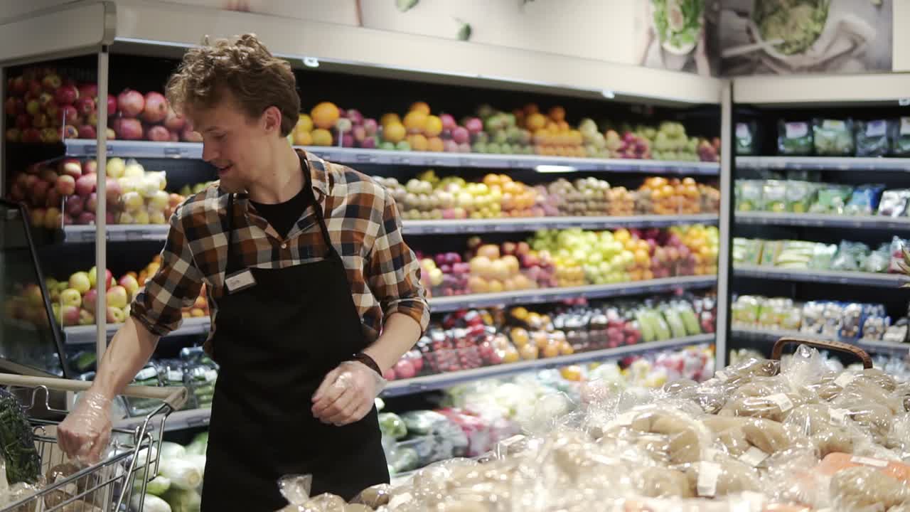 trabajador joven caucásico ocupado organizando verduras en los estantes de la tienda de comestibles. hombre en delantal llenando el estante de almacenamiento con papas orgánicas saludables en el supermercado. cámara lenta
