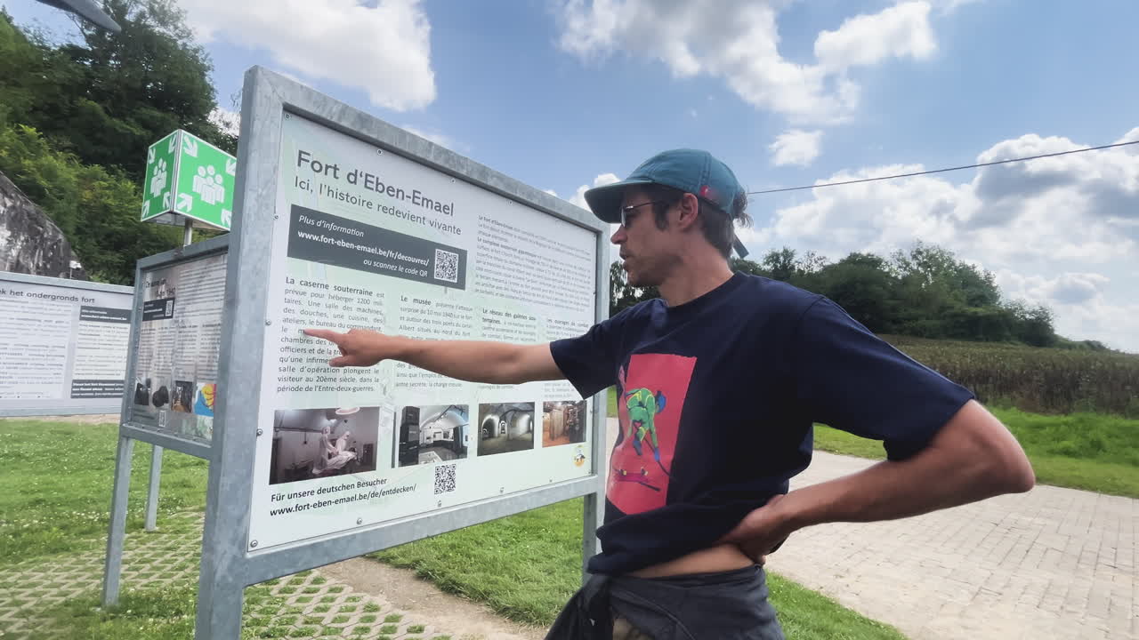Person pointing at informational sign at Fort Eben-Emael, outdoor setting