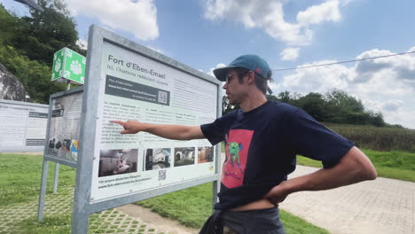 person pointing at informational sign at fort eben-emael, outdoor setting