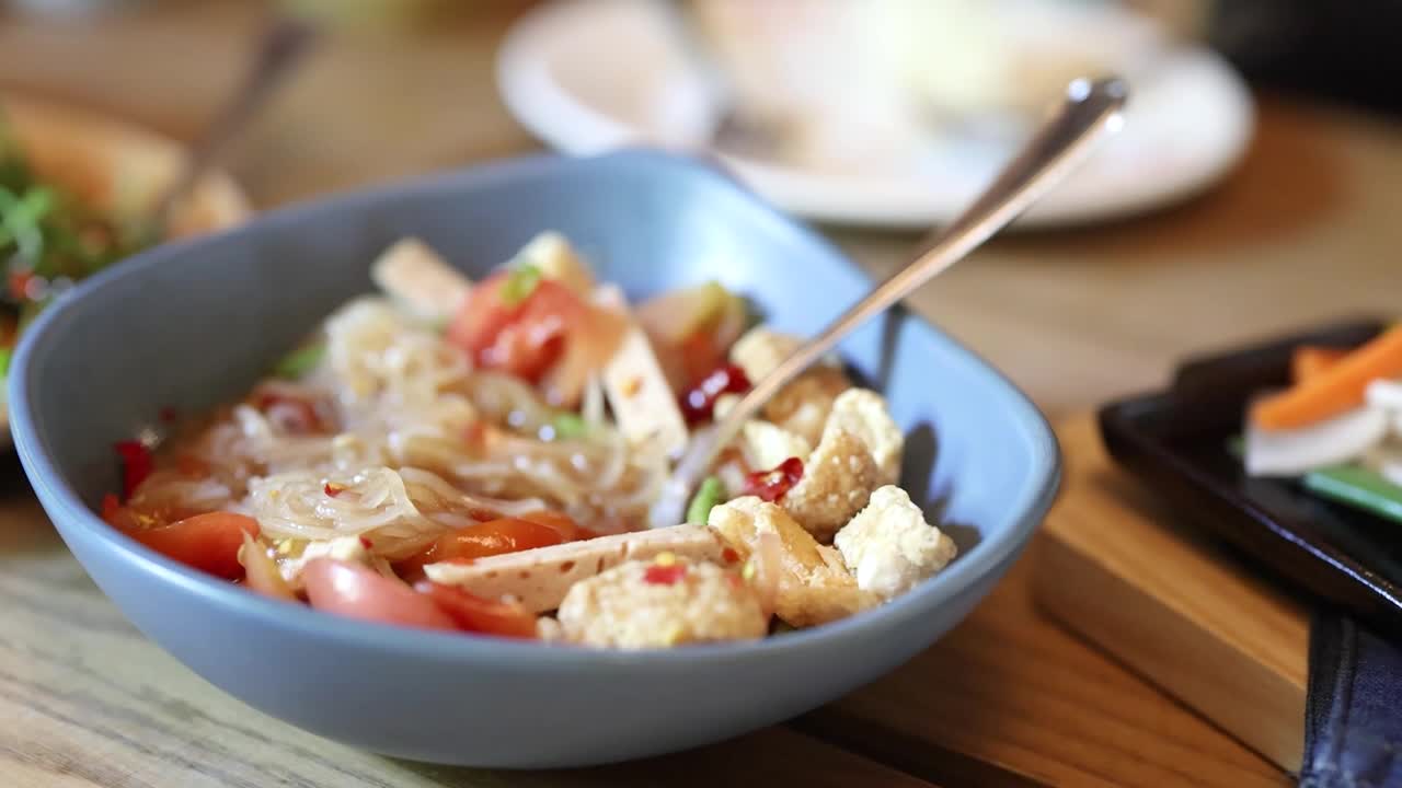 Primo piano di un'insalata di noodles tailandesi piccante con tofu, pomodori e peperoncino in condizioni di illuminazione naturale del ristorante