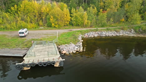 Campervan-Near-Calm-Lakeshore-With-Autumn-Forest-In-The-Background-In-Sweden