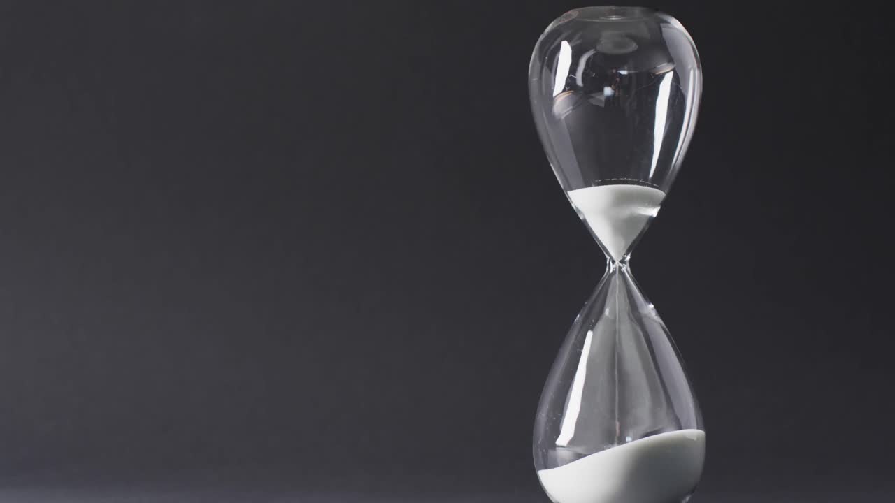 Video of hourglass with sand pouring, copy space on black background