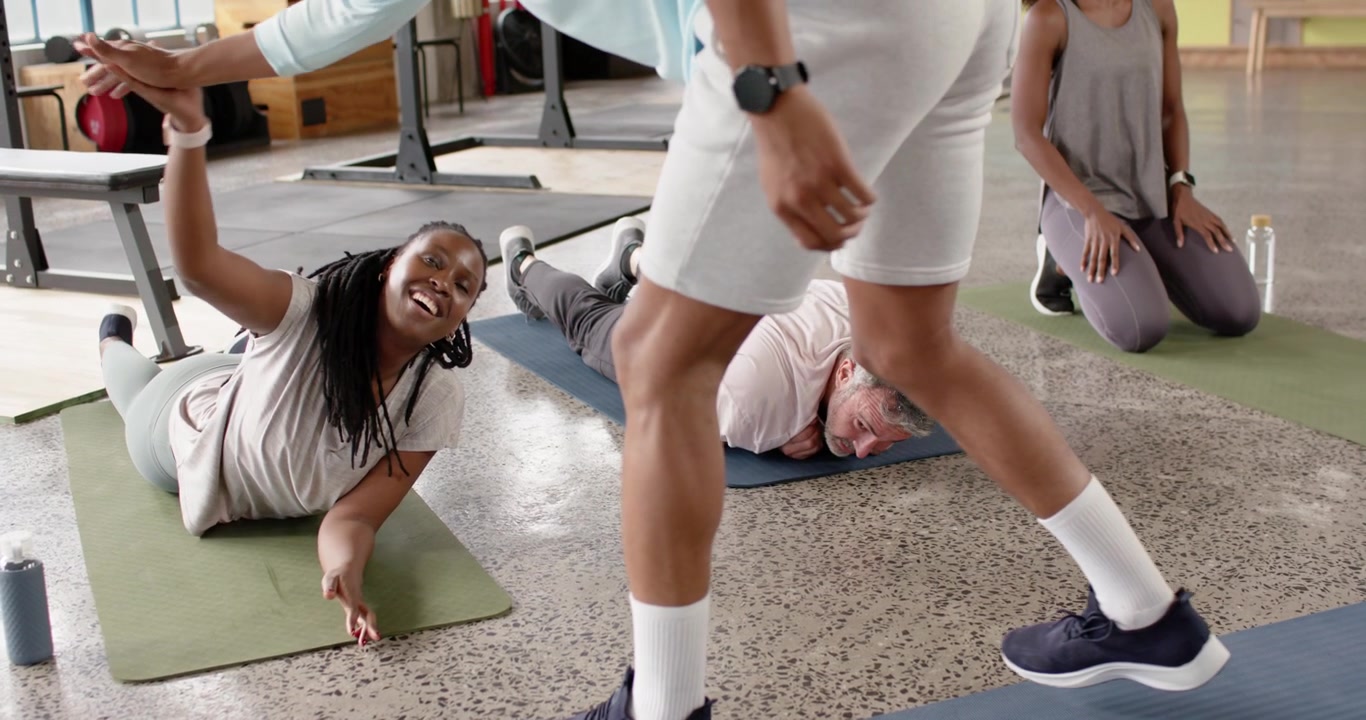 African American woman holding plank on gym mat, relaxing, waving at coach walking by, copy space