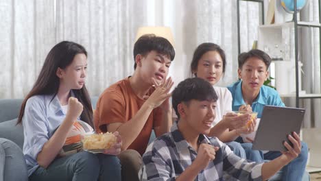 asian teenagers cheering and watching football game on tablet and celebrating victory at home