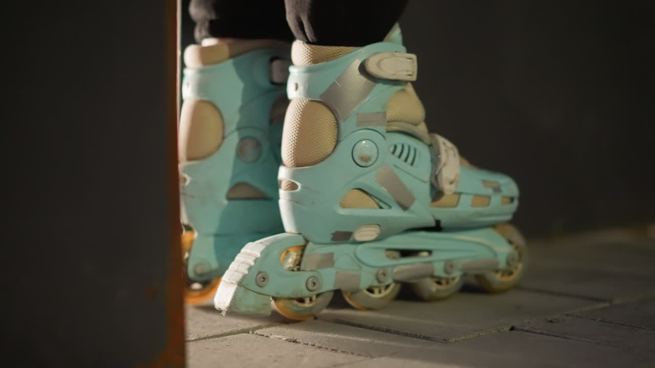 Side view of a pair of blue rollerblades gently rolling in place against a dark nighttime background. The scene highlights the smooth, controlled movement and the details of the rollerblades' design