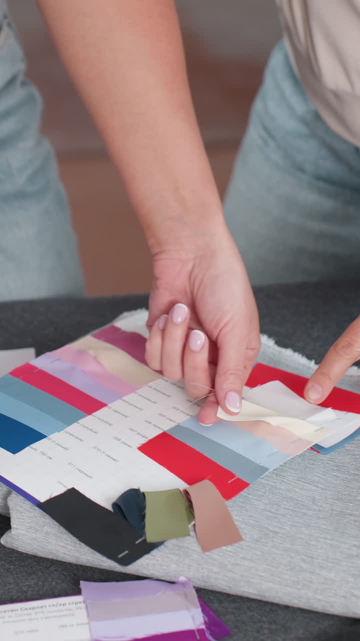 Manos colocando muestras de telas coloridas sobre una mesa, estilista de moda diseñando paletas de colores vibrantes para una colección de temporada, combinando tonos, probando muestras de drapeado y puntadas, ambiente de estudio enérgico