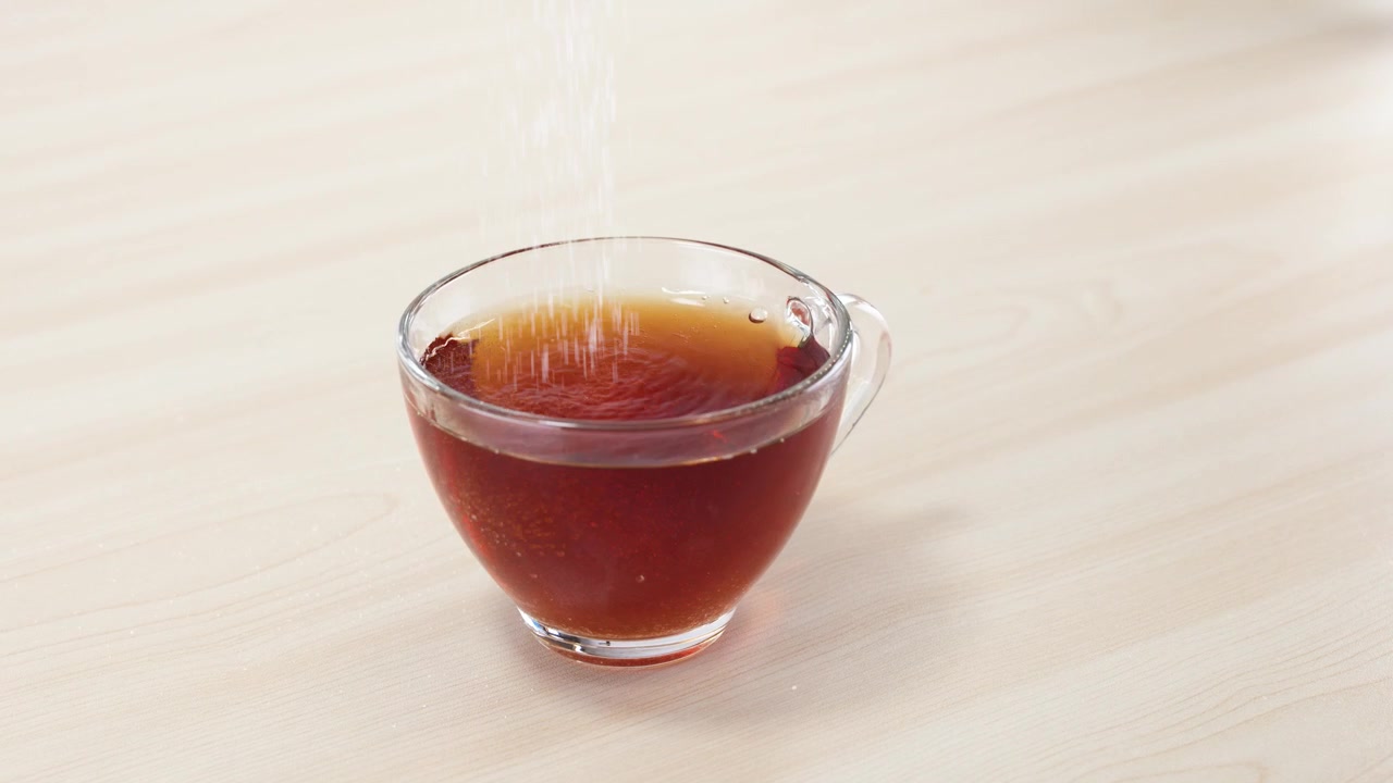 木製のテーブルの上で、熱い紅茶が入ったガラスのカップに白いグラニュー糖が注がれる様子