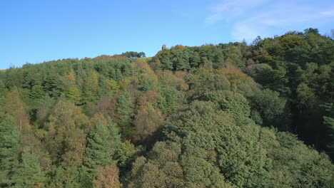 flying over autumnal treetops revealing lone tall tower at hilltop